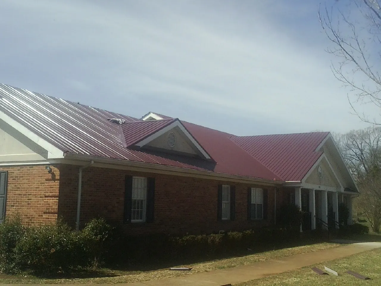 Red metal roof with gabled entries on a long brick building, from a Hail Damage Roof Repair job in Glasgow