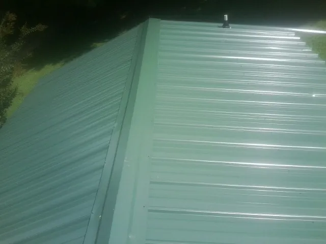 New green metal panels meeting at the ridge of a roof — Flat Roof Repair work by our crew in Glasgow
