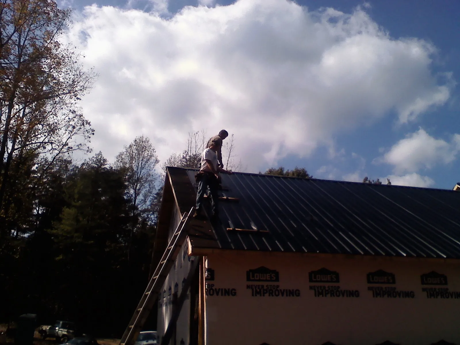 Roofer fastening dark metal panels high against a cloudy sky, from a Roof Inspection job in Glasgow